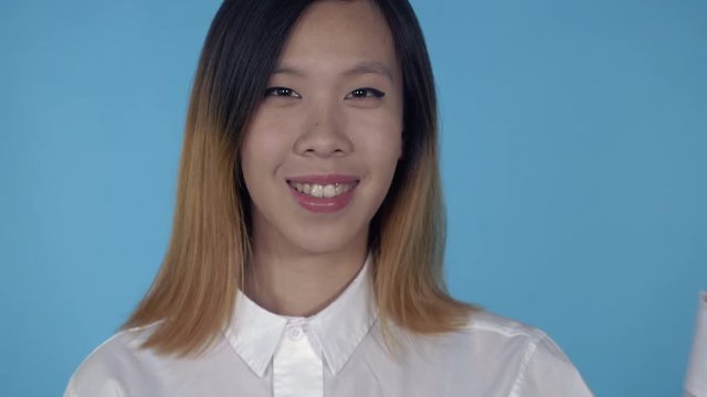 close up portrait young asian woman shows sign symbol victory on blue background in studio. attractive millennial girl looking at the camera smiling