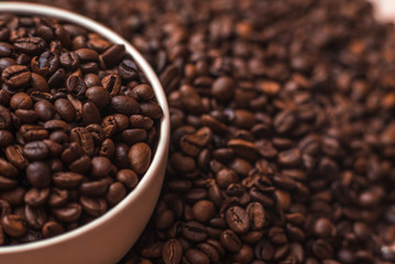 Porcelain cup filled with coffee beans close up on coffee beans background. Beverages menu design. Place for text.