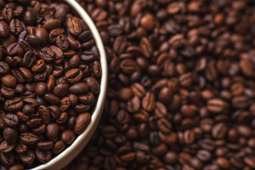 Porcelain cup filled with coffee beans close up on coffee beans background. Beverages menu design. Place for text.
