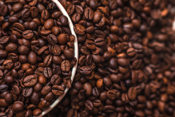 Porcelain cup filled with coffee beans close up on coffee beans background. Beverages menu design. Place for text. Top view.