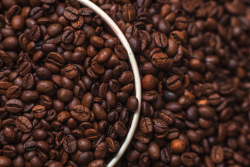 Porcelain cup filled with coffee beans close up on coffee beans background. Beverages menu design. Place for text. Top view.