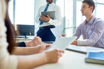 Obraz premium Mid-section view of business people sitting at meeting table in modern office listening to boss during morning briefing