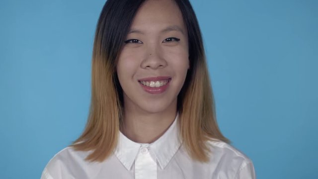 close up portrait young asian woman laughing shows sign hi on blue background in studio. attractive millennial girl looking at the camera