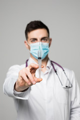 a young doctor in a white coat with a mask on his face holding a syringe is isolated on a white background