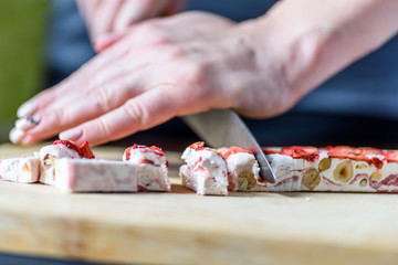 Female Hands Cutting Strawberry Fruit and Nut Nougat with Knife on Wooden Board
