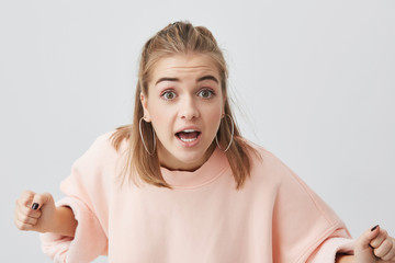 Angry caucasian young female with healthy clean skin wearing pink sweater posing isolated against...