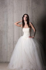 Bride in beautiful wedding dress with off the shoulder poses against the concrete walls. Light make-up and hairstyle