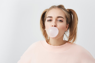 Beautiful, pretty and funny young girl blowing bubble from chewing gum. Blonde female with two...