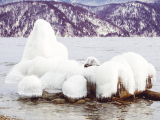 Ice on wooden logs in the water of a winter lake against a background of snow-capped mountains. Teletskoye lake