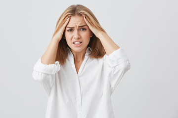 Frustrated young woman having terrible headache keeping hands on head frowning her face with pain looking unhappy and stressful. Female student in despair having stressful situation at university.