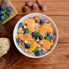 Healthy oatmeal porridge with fresh mandarins, berries, hazelnuts and mint in a white bowl and on a wooden table. Oat recipe for a healthy breakfast. Closeup