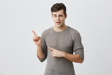 Excited handsome guy indicates with fore finger at copy space for advertisment or promotional text....