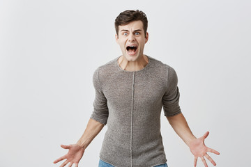 Annoyed caucasian man holds hands in furious gesture, screams loudly as has quarrel with wife,...