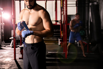 Fototapeta na wymiar Male boxer applying hand wraps while preparing for training in gym