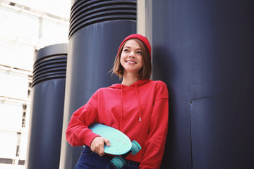 Smiling young woman in red hoodie and beanie holding skateboard, urban lifestyle and youth culture © Africa Studio
