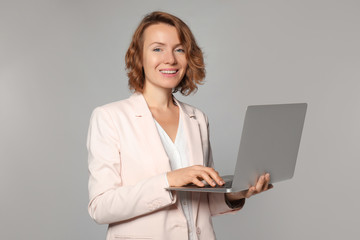 Female manager with laptop on grey background