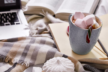 Fototapeta na wymiar Winter mood Christmas Day at home with cup of hot cacao or coffee with marshmallow sweets candy cane and lollipop read book with films at laptop work in the bed with wool knitted plaid New Year.