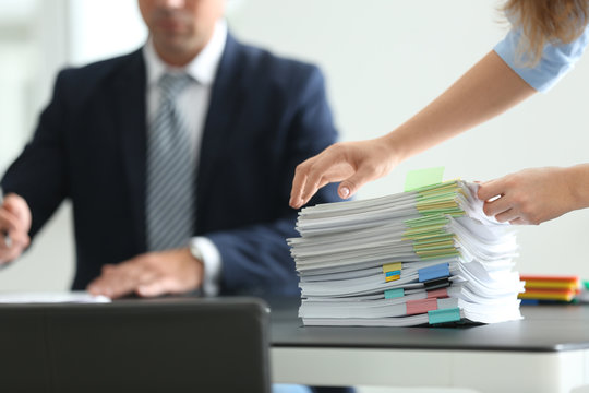Stack of documents on table and office workers indoors