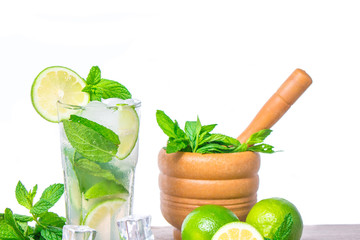 Mojito cocktail with ingredients. Fresh lime, mint leaves and ice cubes, morter with mint and brown sugar on a wooden background. Refreshing alcohol drink. Isolated on white background..