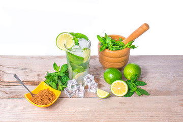 Mojito cocktail with ingredients. Fresh lime, mint leaves and ice cubes, morter with mint and brown sugar on a wooden background. Refreshing alcohol drink. Isolated on white background..