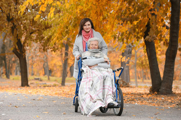 Disabled senior woman and young caregiver in park