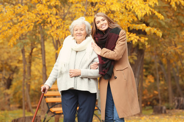 Senior woman with cane and young caregiver in park