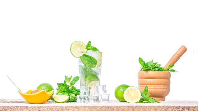 Mojito cocktail with ingredients. Fresh lime, mint leaves and ice cubes, morter with mint and brown sugar on a wooden background. Refreshing alcohol drink. Isolated on white background..