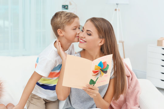 Young woman with her little son and  greeting card for Mother's Day at home