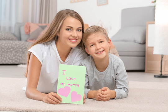 Young woman with her little son and greeting card for Mother's Day at home