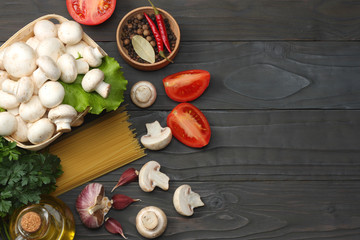 Italian food background, with tomatoes, parsley, spaghetti, mushrooms, oil, lemon, peppercorns on dark wooden table. Top view