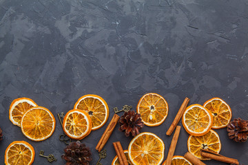 Fototapeta na wymiar Slices of dried orange, cinnamon sticks and pine cones on the dark background.