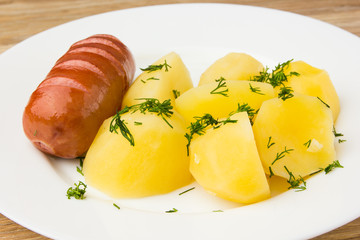 Fried sausage with boiled potatoes. A dish of boiled potatoes and fried sausages on a white plate.