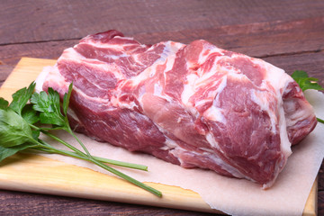 Raw pork neck chop meat with parsley herb leaves on a stone background. Ready for cooking.