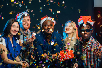 beautiful young friends having fun at New Year's party, wearing santa hats, dancing and blowing...