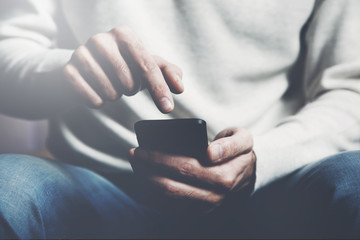 A young man is sitting on a sofa and is using a smart phone