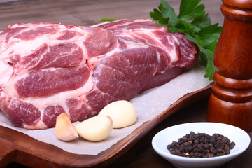 Raw pork neck chop meat with parsley herb leaves, grinder for spices and garlic on a stone background. Ready for cooking.