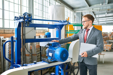 Portrait of successful salesman wearing suit posing next to brand new  machine units  in industrial  showroom
