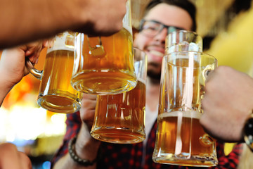Friends clink glasses of beer glasses close-up on the background of the pub