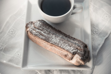 Chocolate eclair on the plate and cup of coffee