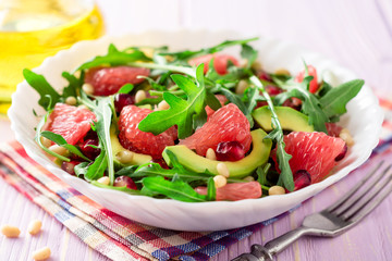 Fresh salad with arugula, grapefruit, avocado, pomegranate seeds and pine nuts.