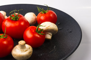 fresh tomatoes and mushrooms - champignons on black plate