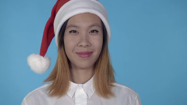 close up portrait young asian woman posing wearing santa claus hat on blue background in studio. attractive millennial looking at the camera