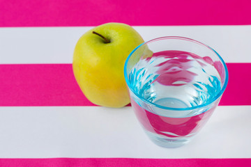 A glass of water and an apple on a tablecloth