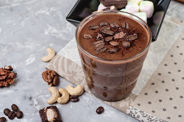 Chocolate smoothie on a glass with coffee beans and nuts on grey stone  background