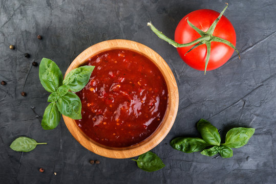 Tomato Ketchup Sauce In A Wood  Bowl With  Herbs And  Tomatoes On Dark Background, Top View