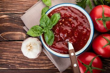 Tomato ketchup sauce in a wood  bowl with  herbs and  tomatoes on rustic background, flat lay.