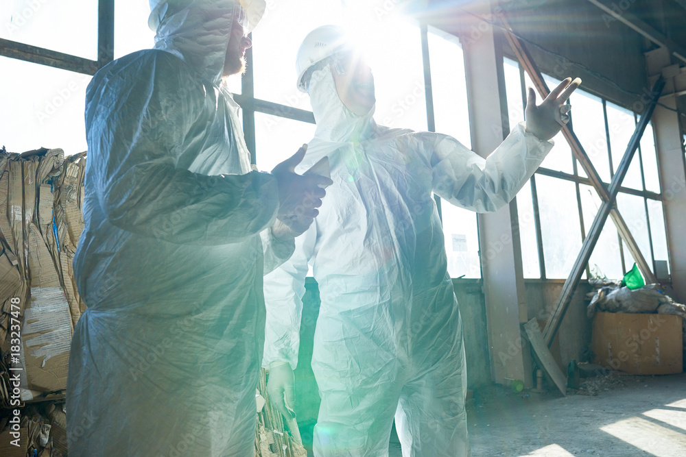 Wall mural portrait of two workers wearing biohazard suits standing in industrial warehouse of modern waste pro