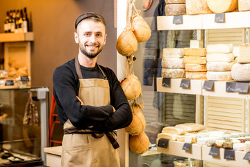 Portrait of a handsome cheese seller in uniform standing near the showcase full of different...
