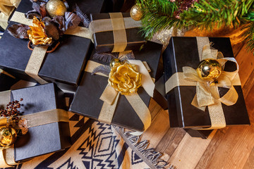 Black paper gift boxes with golden ribbon bow near the Christmas tree. Classic christmas and New Year decorated interior room with presents and New year tree.