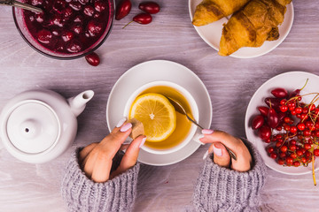 girl's hands with a cup of tea on a background breakfast with croissants and jam - top view